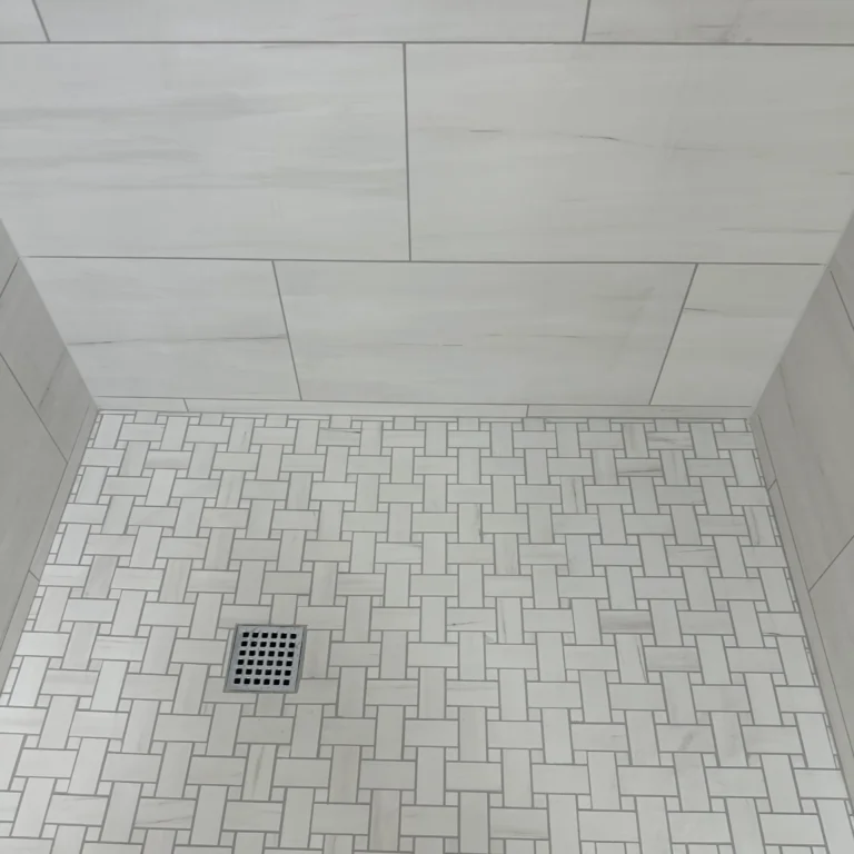 White stone shower with large tiles in the wall and mosaic in the floor for drain.