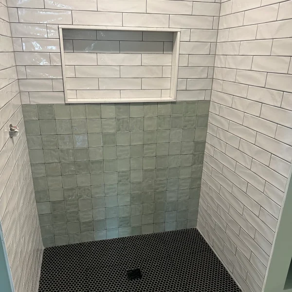 Shower with green square tiles and white rectangular tiles. And a black circle tiles in the floor for the drain.
